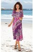 Knielanges Kleid mit halblangen Ärmeln, lila Grundfarbe, pinkes und weißes Paisley-Muster, Rundhalsausschnitt, gerade Form, getragen von lächelnder stehender Frau am Strand