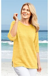 Gelber Pullover mit Rundhalsausschnitt, dreiviertellangen Ärmeln, Seitenschlitzen, getragen von lächelnder stehender Frau am Strand, locker geschnitten