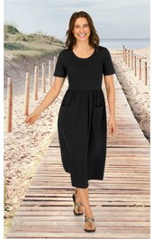 Schwarzes Midikleid mit kurzen Ärmeln, rundem Ausschnitt, tailliert, locker fallend, getragen von stehender Frau auf Holzsteg am Strand