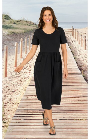 Schwarzes Midikleid mit kurzen Ärmeln, rundem Ausschnitt, tailliert, locker fallend, getragen von stehender Frau auf Holzsteg am Strand