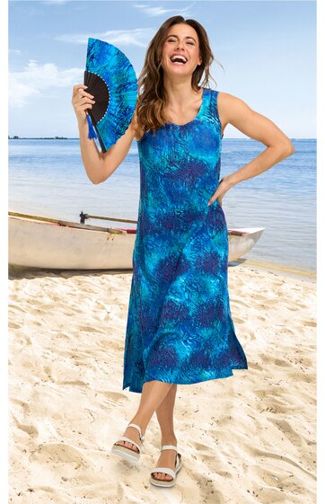 Ärmelloses, knielanges Sommerkleid in Blau mit abstraktem Muster, runder Ausschnitt, figurbetont, getragen von stehender Frau mit Handfächer, Sandstrand und Kanu im Hintergrund