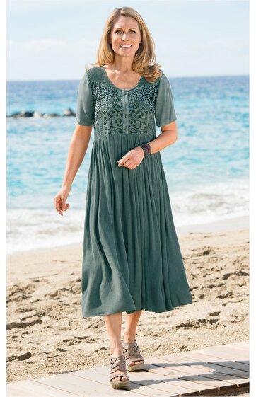 Damenkleid in grünblau, knielang, kurzärmlig, mit rundem Ausschnitt, vorderseitig mit Spitzenmuster und Knopfleiste, weich fallend, getragen von stehender Frau am Strand