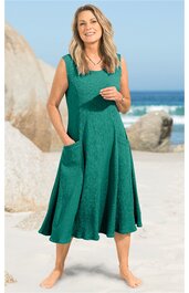 Grünes Midikleid ohne Ärmel, geschwungener Saum, Rundhalsausschnitt, zwei seitliche Eingrifftaschen, getragen von stehender Frau am Strand