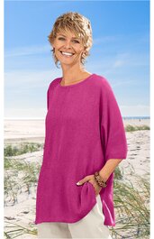 Locker sitzendes, knielanges Damenoberteil in kräftigem Pink, rundhals, halblange Ärmel, Seitenschlitze, getragen von schulterlangen, blonden, lockigen Frau stehend am Strand