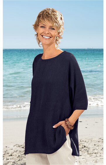 Dunkelblaues, locker geschnittenes Langarmshirt ohne Muster, rundhals, seitliche Taschen, getragen von lächelnder Frau stehend am Strand vor Meer