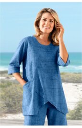 Blaues Zweiteiler-Outfit mit feinem Karomuster, langärmliges Oberteil mit Rundhalsausschnitt, asymmetrischer, spitz zulaufender Saum, seitliche Nahttaschen, weite gerade geschnittene Hose, getragen von stehender Frau am Strand