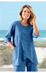 Blaues Zweiteiler-Outfit mit feinem Karomuster, langärmliges Oberteil mit Rundhalsausschnitt, asymmetrischer, spitz zulaufender Saum, seitliche Nahttaschen, weite gerade geschnittene Hose, getragen von stehender Frau am Strand