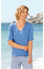 Blaues Kurzarmshirt mit V-Ausschnitt, gerade geschnitten, getragen von stehender Frau, Sandstrand im Hintergrund