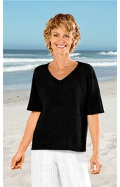 Schwarzes T-Shirt mit V-Ausschnitt, halblangen Ärmeln, gerade geschnitten, getragen von lächelnder Frau stehend am Sandstrand mit Meer im Hintergrund