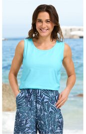 Ärmelloses Top in helltürkis, rundhals, locker sitzend, getragen von lächelnder Frau vor Meereskulisse, dazu blaue Stoffhose mit dunkelblauem und weißem Blattmuster, elastischer Bund