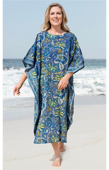 Blaues Kaftankleid mit floralen gelben und grünen Mustern, rundem Ausschnitt, weitem Schnitt, kurze Ärmel, getragen von lächelnder stehender Frau am Strand, knöchellang