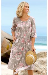 Midikleid beige mit rosa Blumenmuster, Rundhalsausschnitt mit Knopfverschluss, halblange Ärmel, Falten vorne, seitliche Eingrifftaschen, ausgestellte Form, gehalten von stehender Frau, Strandhintergrund