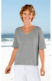 Hellgraues Kurzarmshirt ohne Muster, V-Ausschnitt, gerade geschnitten, getragen von stehender Frau vor Strandhintergrund