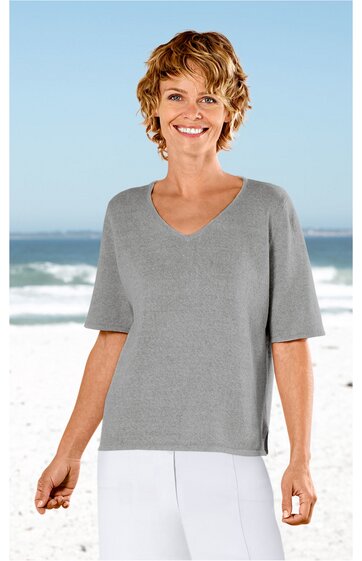 Hellgraues Kurzarmshirt ohne Muster, V-Ausschnitt, gerade geschnitten, getragen von stehender Frau vor Strandhintergrund