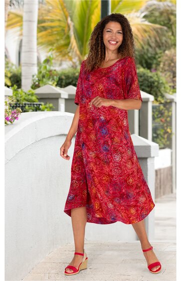 Rotes midikleid mit floralem allovermuster, v-ausschnitt, kurzärmlig, leichter asymmetrischer saum, getragen von stehender frau mit schulterlangen lockigen haaren, kombiniert mit roten sandaletten mit absatz