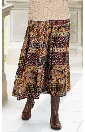 Maxirock mit buntem Patchwork-Muster in Braun-, Rot- und Beigetönen, elastischer Bund, weite Form, getragen von stehender Person mit beigefarbenem Strickpullover und braunen Stiefeln