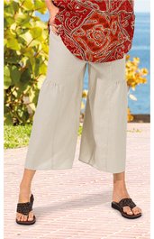 Helle Culotte-Hose in Beige, weit geschnitten mit angesetzten Volants am unteren Beinabschluss, getragen von stehender Person, kombiniert mit schwarzem, geflochtenem Sandalenpaar