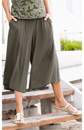 Helle olivgrüne Culotte-Hose, knielang, weit geschnitten, mit seitlichen Eingrifftaschen, getragen von stehender Person, kombiniert mit Sandalen und gemustertem Oberteil