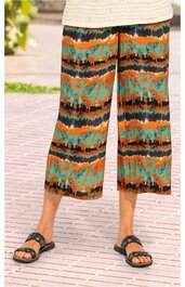 Hose in Capri-Länge, buntes abstraktes Muster in Orange, Schwarz und Grün, lockerer Schnitt, getragen von stehender Person, elastischer Bund