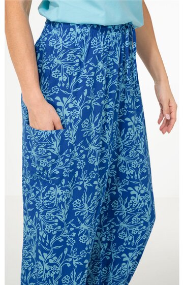 Locker sitzende Hose in Blau mit hellblauem Blumenmuster, elastischer Bund, seitliche Tasche, getragen von Person mit heller Haut, obere Körperhälfte teilweise sichtbar