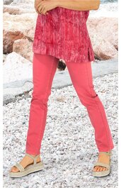 Korallenrote Hose, einfarbig, gerade geschnitten, mittelhohe Taille, getragen von stehender Person mit übereinandergeschlagenen Armen, kombiniert mit rotem Oberteil mit feinem Muster und Sandalen in Beige