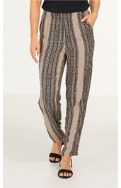 Bequeme Stoffhose in Beige mit schwarzen vertikalen Streifen und feinem geometrischem Muster, gerade geschnitten, hoher Bund, seitliche Eingrifftaschen, getragen von stehender Person mit schwarzem Top und schwarzen offenen Sandalen