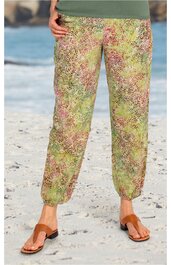 Leichte lange Hose in hellgrün mit feinem mehrfarbigem Blumenmuster, gerade geschnitten, mit elastischem Bund und Bündchen, getragen von stehender Person am Strand, kombiniert mit braunen Sandalen