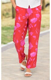 Rote Damenhose mit pinkem Blumenmuster, gerade geschnitten, hoher Bund, getragen von stehender Person, kombiniert mit weißen Riemchensandalen