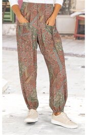 Locker geschnittene Hose mit Paisley-Muster in Braun- und Grüntönen, elastischer Bund und Fußabschlüsse, seitliche Eingrifftaschen, getragen von Person im Stehen mit weißen Sneakern