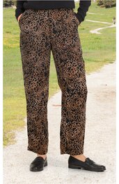 Person trägt schwarze Schuhe und braune Hose mit schwarzem Muster, stehend auf einem Weg im Freien