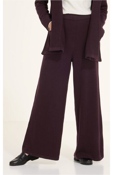 Weite Hose in dunklem Aubergine, ohne Muster, hoher Bund, gerade geschnitten, getragen von stehender Person, kombiniertes Outfit mit gleichfarbiger Jacke und weißen Oberteil