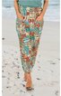 Locker sitzende lange Hose in Beige mit blau-rotem Patchwork-Muster, elastischer Bund, seitliche Eingrifftaschen, getragen von stehender Person am Strand