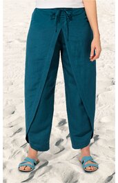 Hose in dunklem Petrolblau, lockere Passform, weites Bein, sichtbare Kellerfalte vorne, hoher Bund mit Kordel zum Binden, getragen von stehender Person am Strand, Fußknöchel frei, kombiniert mit offenen hellblauen Sandalen