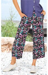 Weite, knöchellange Hose mit abstraktem Muster in Schwarz, Pink, Türkis und Hellgrau, elastischer Bund, seitliche Eingrifftaschen, getragen von stehender Person mit Händen in den Taschen, kombiniert mit lila Oberteil und weißen Sneakers