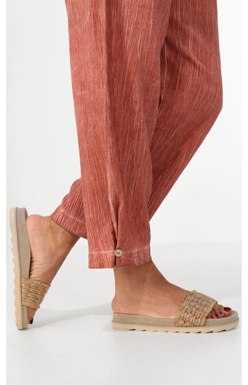 Hose rostrot mit feiner Längsstruktur, gerader Schnitt, Beinabschluss mit kleiner Schlaufe und Knopf, getragen von Person mit Sandalen aus geflochtenem Naturmaterial, offene Zehen