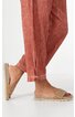 Hose rostrot mit feiner Längsstruktur, gerader Schnitt, Beinabschluss mit kleiner Schlaufe und Knopf, getragen von Person mit Sandalen aus geflochtenem Naturmaterial, offene Zehen