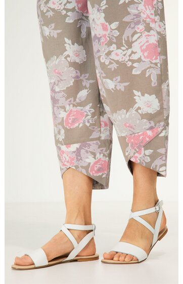 Beige Caprihose mit rosa und weißen Blumenmuster, gerade geschnitten, endet knapp oberhalb der Knöchel, getragen von stehender Person, weiße flache Sandalen mit Kreuzriemen und Knöchelriemen