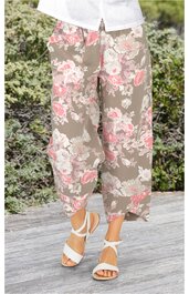 Bequeme, weit geschnittene Damenhose in olivgrün mit großem rosa-weißem Blumenmuster, knöchellang, elastischer Bund, getragen von stehender Person mit weißen Sandalen