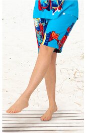 Blaues Damen-Shorts mit buntem abstraktem Muster, gerade geschnitten, knielang, getragen von stehender Person mit gekreuzten Beinen, sommerlich, leichtes Material erkennbar