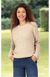 Beiger Grobstrickpullover mit runder Halsöffnung, lange Ärmel, gerader Saum, getragen von lächelnder stehender Frau mit Händen in den Hosentaschen, kombiniert mit blauen Jeans