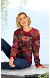 Rotes Damenpullover mit buntem Blumenmuster, Rundhalsausschnitt, lange Ärmel, gerade geschnitten, getragen von sitzender Frau mit blonden Haaren in entspannter Pose, dunkelblaue Jeans