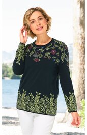 Dunkelgrüner Pullover mit buntem Blumenmuster an Schultern und unteren Ärmeln, Rundhalsausschnitt, lange Ärmel, gerade geschnitten, getragen von stehender Frau mit weißen Hosen