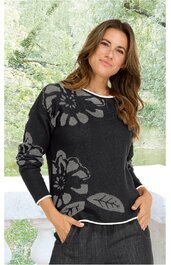 Schwarzer Pullover mit großflächigem grauem Blumen- und Blättermuster, Rundhalsausschnitt mit weißem Saum, lange Ärmel, getragen von stehender Frau mit Händen in Taschen