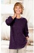 Dunkellila langärmeliges Pullover-Shirt, rundhalsausschnitt, locker geschnitten, getragen von lächelnder stehender Frau mit kurzer blonder Frisur, eine Hand im Hosenbein, helle Hose