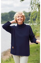 Damenpullover in dunkelblau, langer, weiter Schnitt, Stehkragen, dekorative große Knöpfe an der linken Hüftseite, getragen von stehender Frau mit rechter Hand am Nacken und linker Hand seitlich ausgestreckt