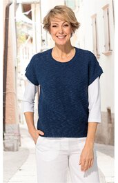 Dunkelblaues, kurzärmliges Strickoberteil mit Rundhalsausschnitt, unifarben, getragen von stehender Frau mit weißen langen Ärmeln und weißer Hose, entspannte Passform