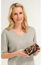 Beige Pullover mit kurzem Ärmel, V-Ausschnitt, getragen von lächelnder Frau mit schulterlangem blonden Haar, sie hält schwarze rechteckige Geldbörse mit orange-rotem Muster und Reißverschluss