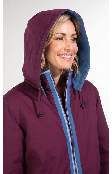 Damenjacke in dunklem Aubergine mit Kapuze, Kapuzeninnenseite und Reißverschlussumrandung in Hellblau, stehender Kragen, Reißverschluss vorne, getragen von lächelnder Frau in halber Nahaufnahme, Kapuze aufgesetzt