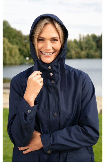 Dunkelblaue Regenjacke mit Kapuze, durchgehender Knopfleiste mit sechs schwarzen Knöpfen, elastische Ärmelbündchen mit Knopfverschluss, getragen von lächelnder Frau, stehende Frontansicht, Outdoor-Hintergrund