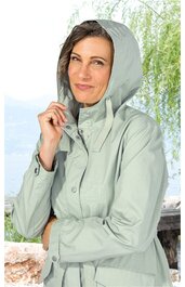 Hellgraue, langärmelige Regenjacke mit Kapuze, verdeckter Knopfleiste, Stehkragen, lockere Passform, getragen von stehender Frau vor Wasser- und Baumkulisse
